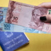 Carteira de trabalho e Previdência Social em um fundo amarelo, com mão segurando notas de dinheiro.