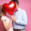 Casal se beijando escondidos atrás de um balão em forma de coração.