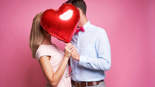 Casal se beijando escondidos atrás de um balão em forma de coração.