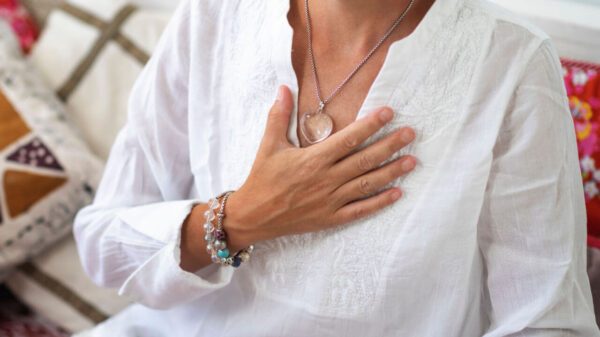 Meditação de autocura do chakra do coração. Mulher sentada em posição de lótus com a mão direita no chakra do coração. Despertar espiritual.