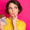 Retrato de mulher comendo chocolate, isolada sobre um fundo rosa.