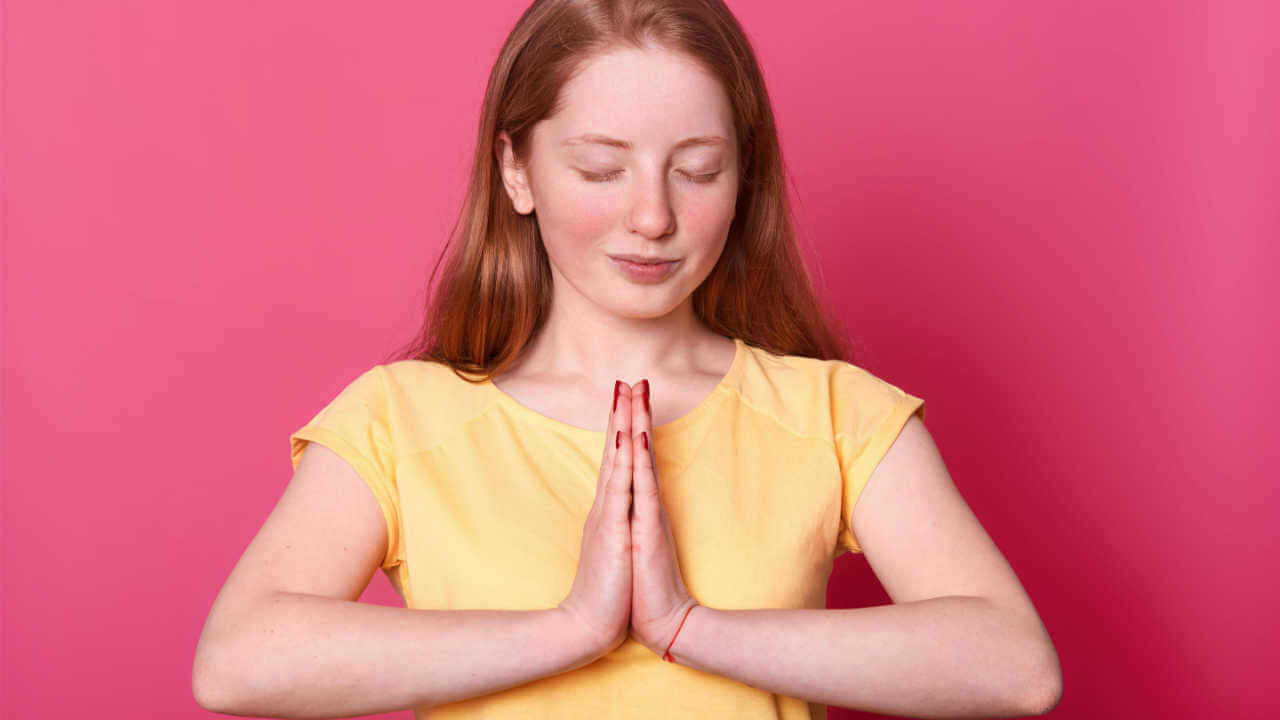 Foto de estúdio de uma adolescente calma, isolada sobre fundo rosa enquanto ora, com os olhos fechados, pedindo algo importante para ela, usando camiseta casual amarela.