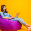 Foto de mulher alegre, positiva, navegando através de seu laptop, sobre fundo amarelo.