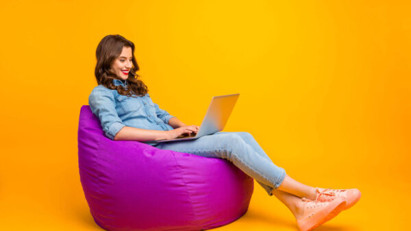 Foto de mulher alegre, positiva, navegando através de seu laptop, sobre fundo amarelo.