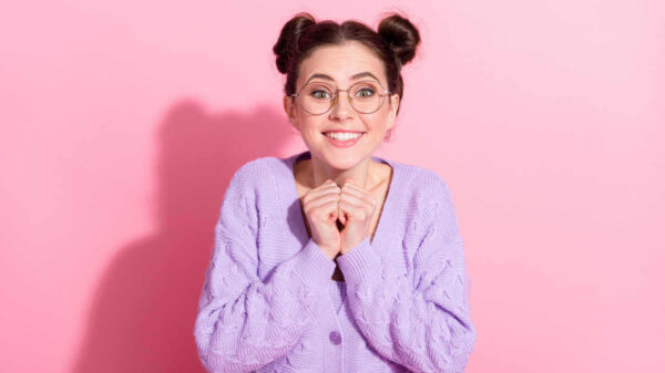 Retrato fotográfico de uma garota alegre e feliz, usando óculos, sorrindo, isolada em fundo de cor rosa pastel.