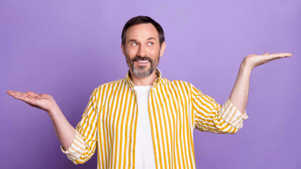 Foto de um homem feliz, olhando para o lado, fazendo gesto de equilíbrio, em fundo de cor lilás.