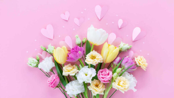 Buquê de flores da primavera e corações de papel na mesa rosa pastel para Dia das Mães.