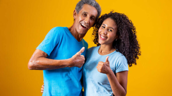 Pai e filha em fundo amarelo, com o polegar para cima fazendo sinal positivo de "ok".