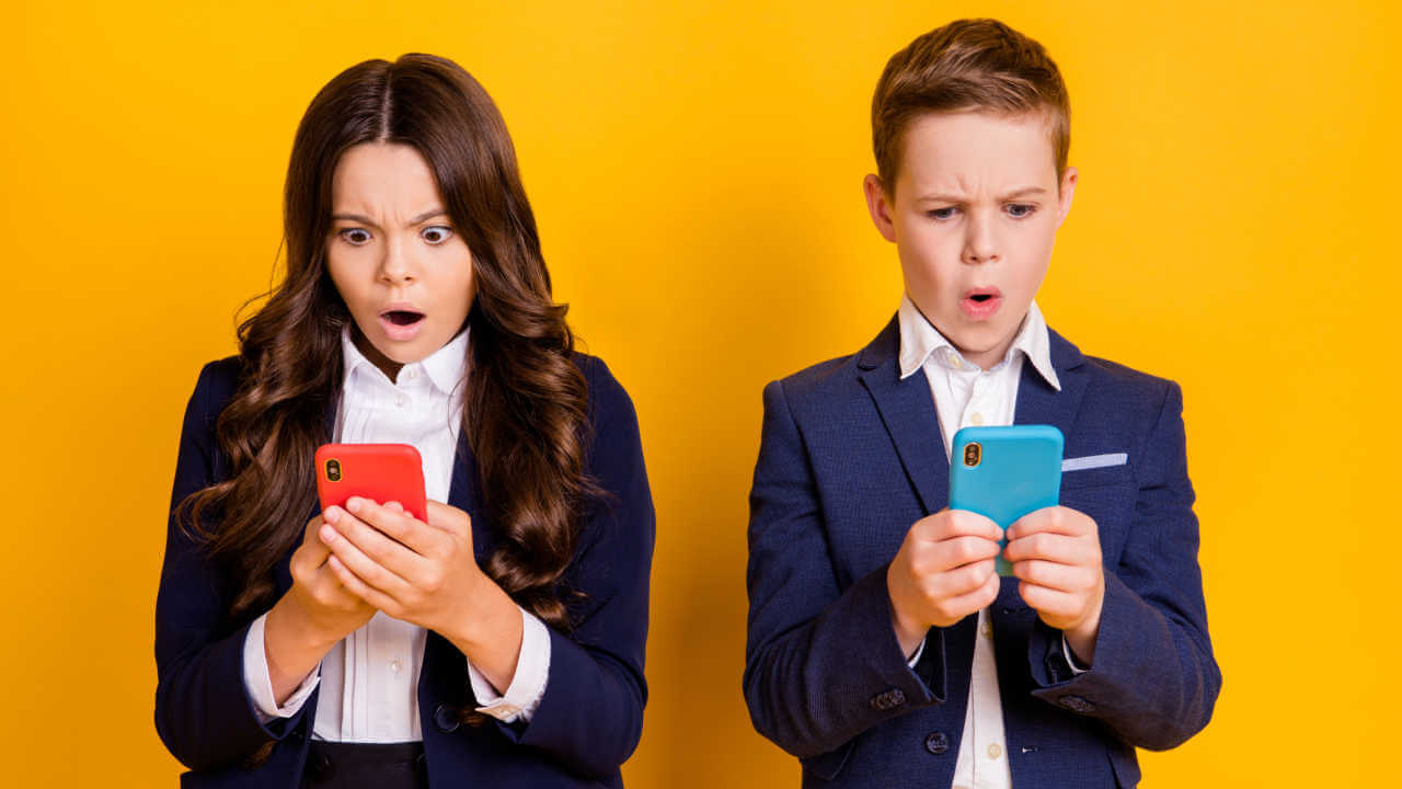 Retrato de menino e menina atordoados, preocupados, indignados. Crianças usando celular, lendo notícias falsas, isolados em um fundo de cor amarela.