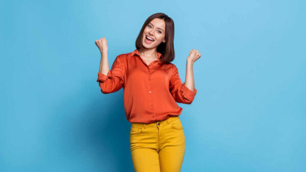 Foto de uma jovem animada e alegre, regozijando-se, com as mãos indicando sucesso, isolada sobre um fundo de cor azul.