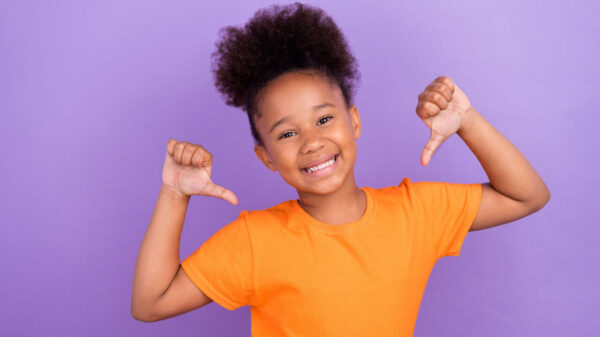 Foto de uma gratoinha jovem e alegre, feliz, sorrindo positivamente, apontando os polegares para si mesma, orgulhosa de si, isolada sobre um fundo de cor violeta.