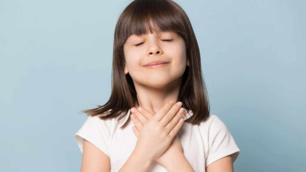Foto de menina de cabelos castanhos, com os olhos fechados, com as mãos no peito. Símbolo de sentimentos profundos de gratidão. Isolada em fundo azul.