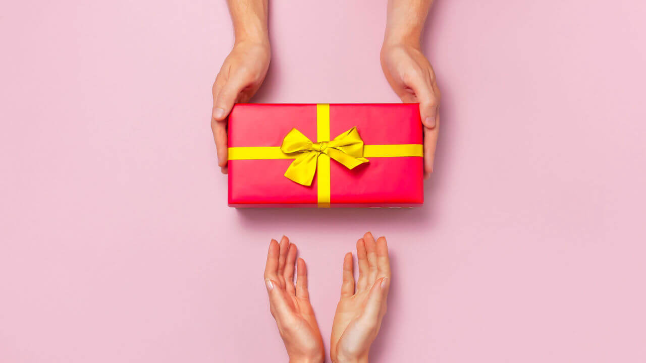 Vista superior de mãos segurando caixa de presente vermelha, com fita amarela, em um fundo rosa. Conceito de presente de, Dia dos Namorados.