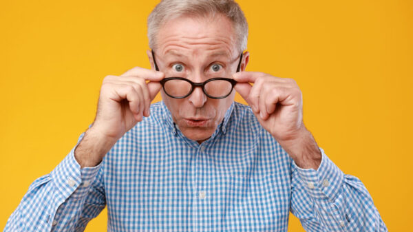Retrato aproximado de um homem surpreso, olhando para a câmera, tirando os óculos, isolado em um fundo de um estúdio laranja.