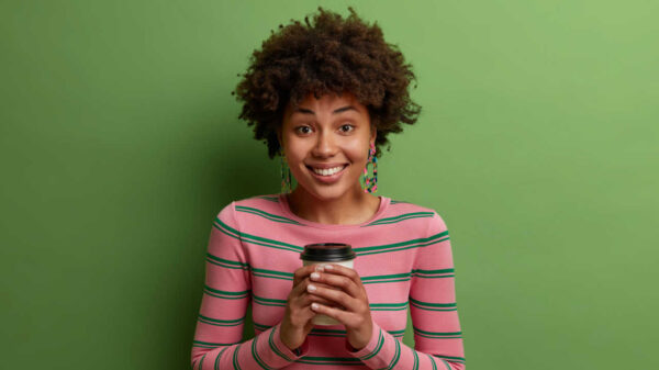 mulher negra segurando um copo de café e sorrindo em fundo verde
