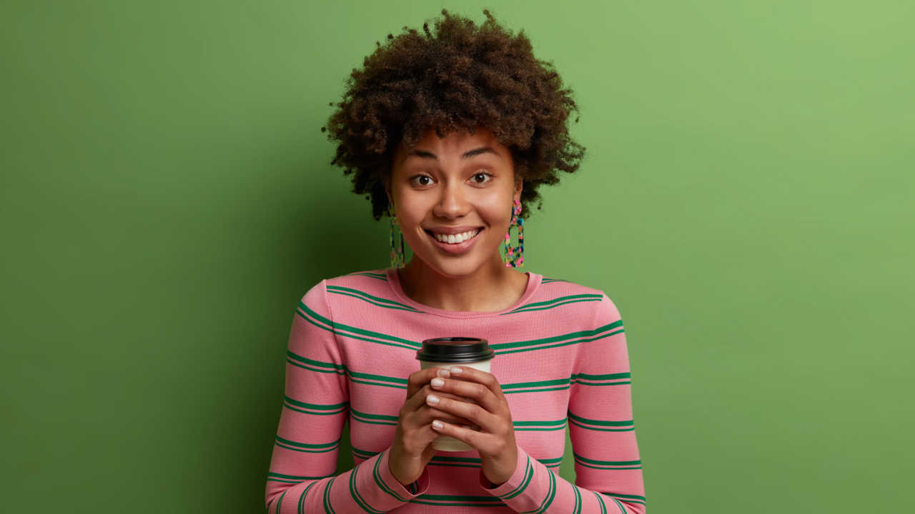 mulher negra segurando um copo de café e sorrindo em fundo verde