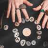 Astrologia e esoterismo. Mãos femininas sobre um círculo rúnico. Runas de adivinhação sobre um fundo preto, livros, amuletos preciosos, uma lâmpada de cobre e uma vela.
