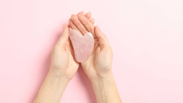 cristal de quartzo rosa em formato de coração na palma de um par de mãos em fundo rosa