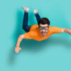Foto do corpo inteiro de um jovem animado e positivo, usando óculos, saltando de um pára-quedas, pára-quedista, em queda livre, isolado em fundo de cor água-marinha.