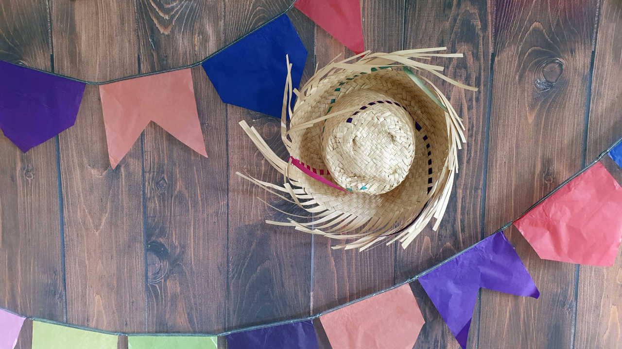 bandeirinhas coloridas em fundo de madeira com um chapéu de palha no centro direito