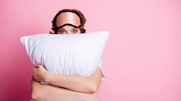 mulher de cabelo curto segurando um travesseiro branco na altura dos olhos em fundo rosa