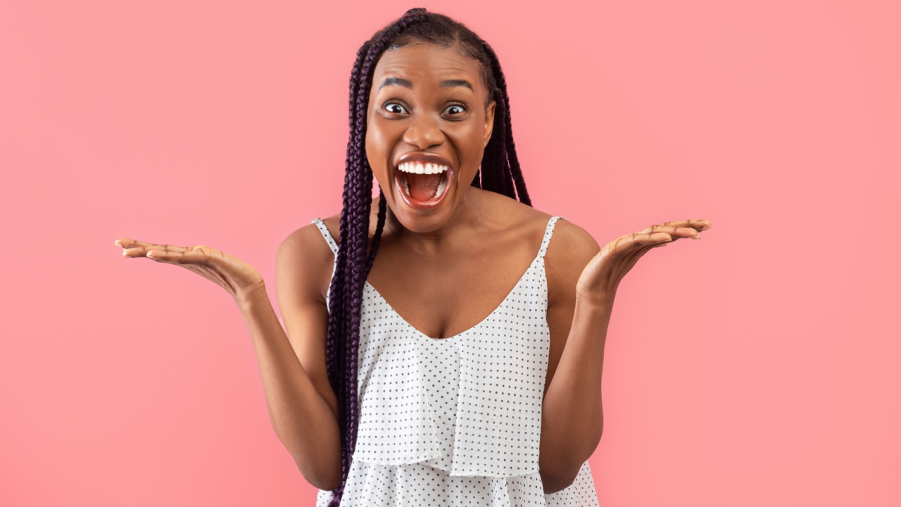 mulher negra com expressão de felicidade. Ela veste roupa branca e o fundo da imagem é rosa