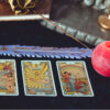 Três cartas de tarot e uma vela vermelha em uma mesa com pano preto