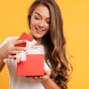 Retrato de uma menina sorridente, feliz, abrindo uma caixa de presente, isolada sobre fundo amarelo.