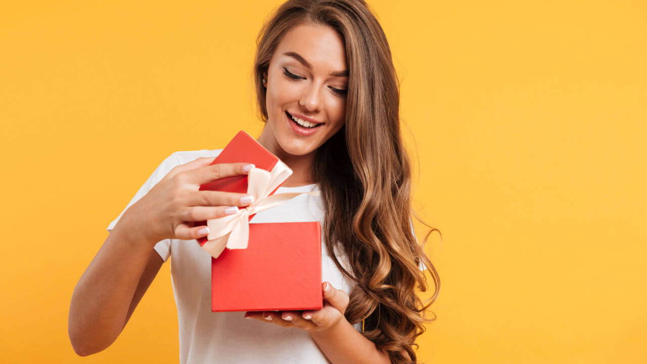 Retrato de uma menina sorridente, feliz, abrindo uma caixa de presente, isolada sobre fundo amarelo.