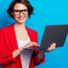 Retrato de mulher alegre, segurando na mão um laptop, isolada em um fundo de cor azul.