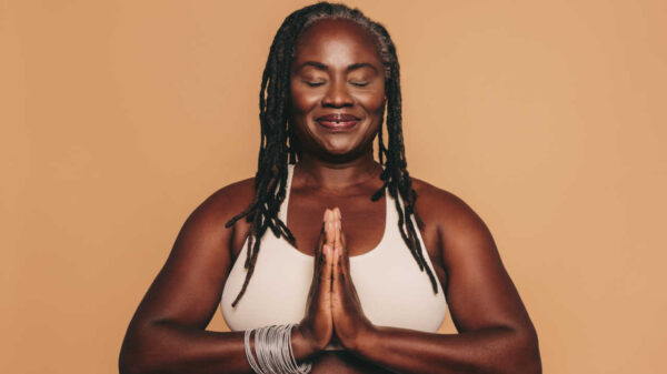 mulher negra de tranças com com as mãos juntas e roupas de ioga em fundo marrom