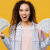 imagem de uma mulher vestindo camisa xadrez e segurando dois leques de dinheiro, um cada mão. O fundo é amarelo