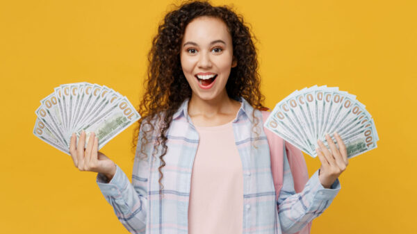 imagem de uma mulher vestindo camisa xadrez e segurando dois leques de dinheiro, um cada mão. O fundo é amarelo