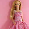 Barbie usando um vestido, posando contra um fundo rosa.