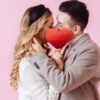 Beijo de um casal escondido por um coração vermelho de papel.