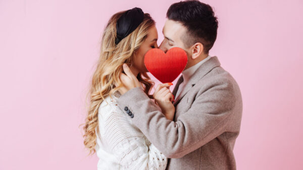 Beijo de um casal escondido por um coração vermelho de papel.