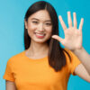Mulher alegre, com a palma da mão levantada fazendo o número cinco, sorrindo alegremente, em um fundo azul.