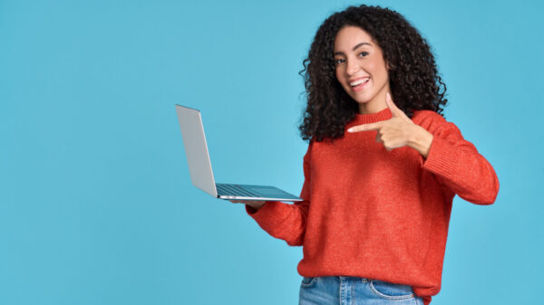 Mulher jovem, feliz, apontando para um laptop, isolada em fundo azul. Mulher sorridente segurando um computador.