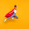 Mulher alegre, pulando, usando uma capa vermelha, voando, isolada em um fundo de cor amarela.