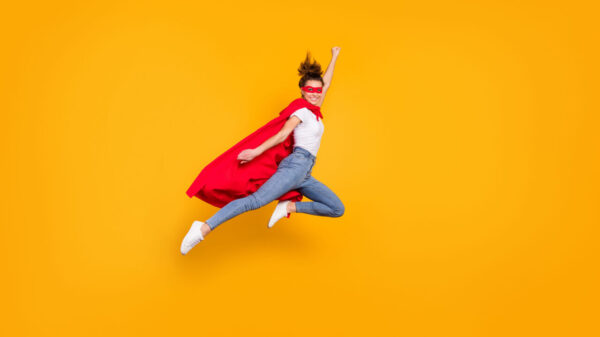 Mulher alegre, pulando, usando uma capa vermelha, voando, isolada em um fundo de cor amarela.