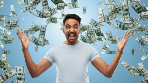 Homem feliz, celebrando algum triunfo, sobre um fundo azul com notas de dinheiro caindo. Conceito de sucesso, riqueza e finanças.