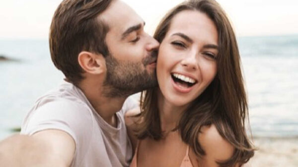 selfie de casal. o homem, à direita, está beijando a bochecha da mulher