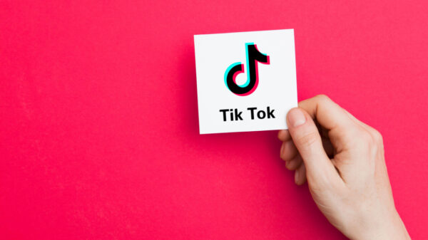 uma mão segurando um cartão com a logo do aplicativo tik tok em fundo pink