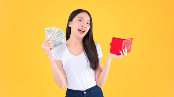 mulher branca com roupa também branca segurando um leque de dinheiro na mão direita e uma carteira vermelha na mão esquerda em fundo amarelo