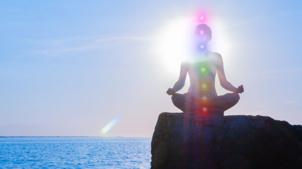 mulher meditando em frente ao mar. nela foi inserido digitalmente as marcas dos sete chakras