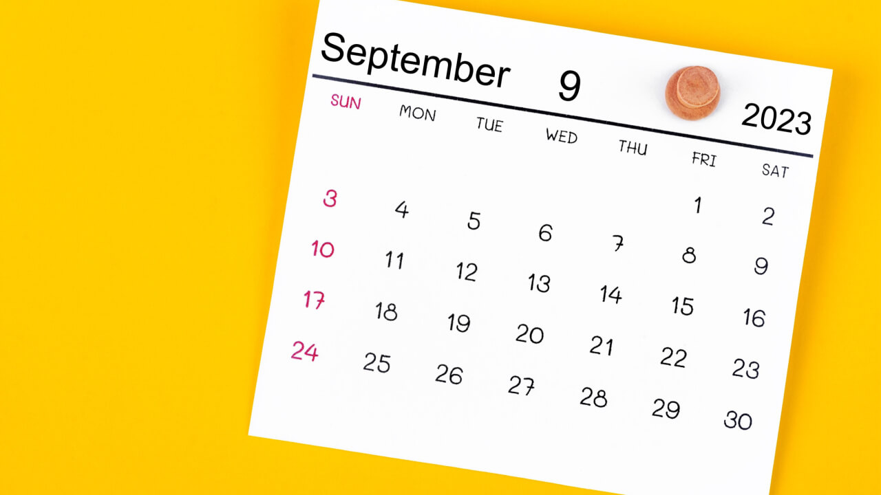 Calendário de setembro de 2023 preso por um alfinete de madeira, sobre um fundo amarelo.