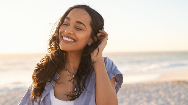 mulher negra com uma blusa branca e uma camisa azul sorrindo na praia