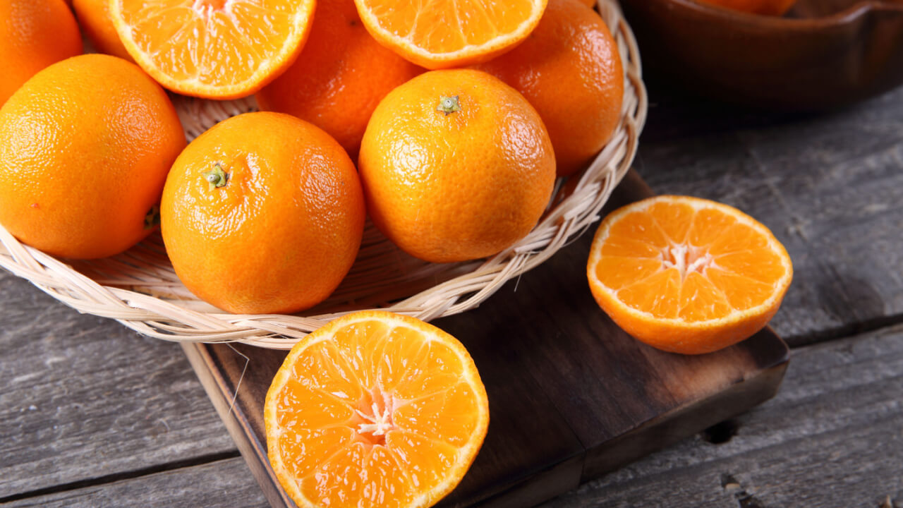 cesto com laranjas. fora do cesto, em uma mesa de madeira, há uma laranja cortada ao meio