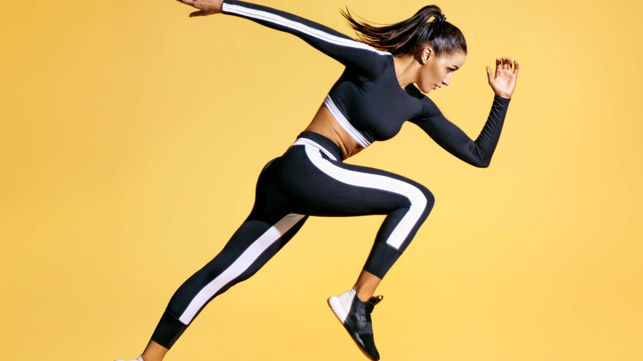 Mulher correndo, sobre um fundo amarelo, usando roupas esportivas. Vista lateral.