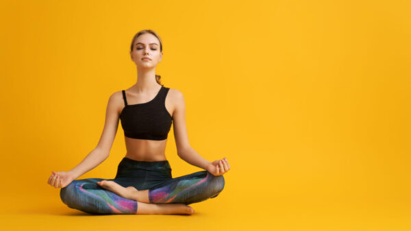 Mulher praticando ioga e fazendo meditação em um fundo de cor amarela.